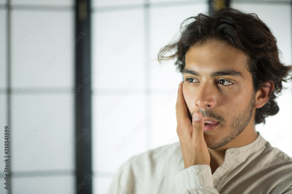 An handsome young man, 20Y, is posing in studio and touching his chin in doubt. White skirt. Retroilluminated booths in the background. An handsome young man, 20Y, is posing in studio and touching his chin in doubt. White skirt. Retroilluminated booths in the background.