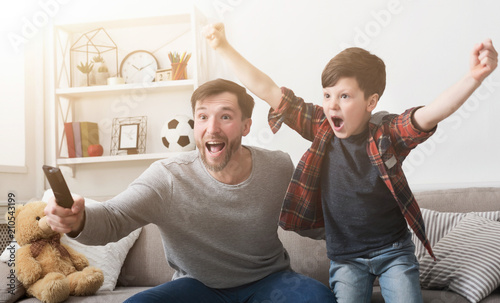 Father and son watching football on TV at home.