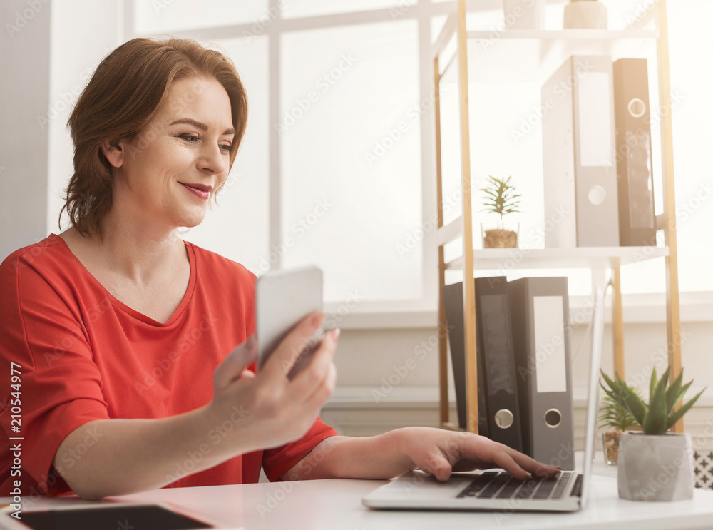 Businesswoman typing on laptop and using smartphone in office Businesswoman typing on laptop and using smartphone in office