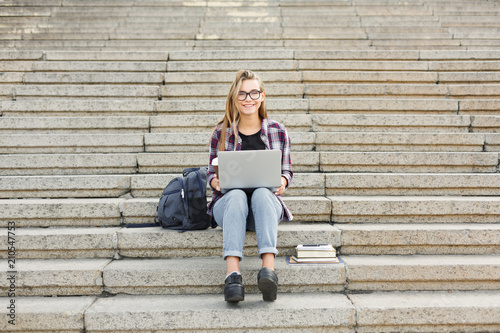Happy student sitting on stairs using laptop