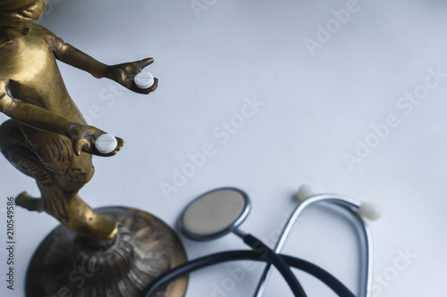 bronze statue holds two white tablets in hands on the gray background with stethoscope..anthropomorphic hands holding pills with space for text