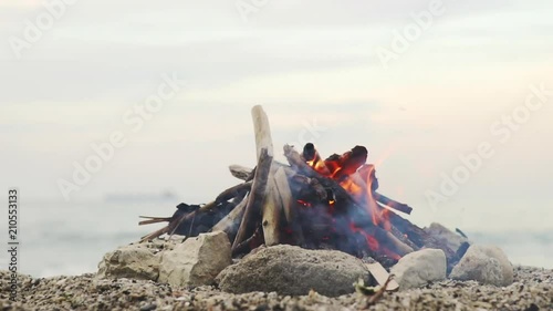 The sea view. Slow motion a bonfire in the flint of rock stones. A bright fire of a flame in a beautifully built tourist campfire on the sand against the backdrop of a small wave on the sea at sunset