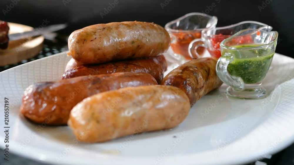 Cooking in a grill sausages lie on a plate near several sauces. Meat dishes from a barbecue. Cooking in a grill sausages lie on a plate near several sauces. Meat dishes from a barbecue.