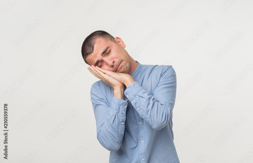 Young man wearing a blue outfit putting his palms like a pillow. Looking sleepy and tired. Young man wearing a blue outfit putting his palms like a pillow. Looking sleepy and tired.
