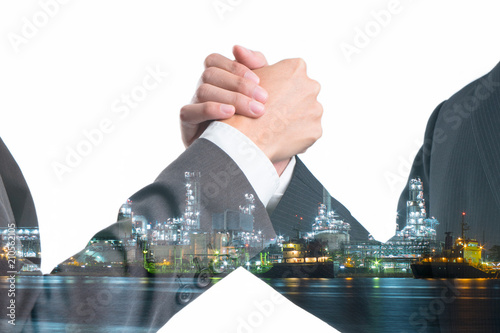 Double exposure of Business people gripping hands on Power plant with shipping boat at night time.  Investment in Energy concept.