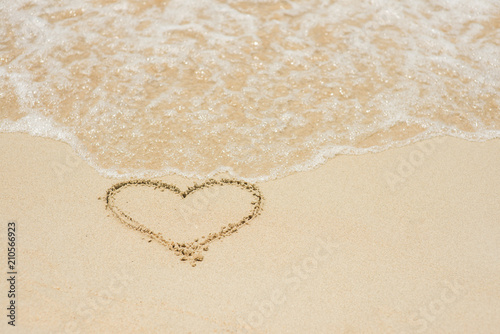 Heart symbol on a sand of beach with wave.