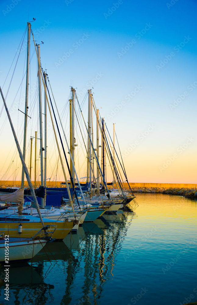 Overview of different sailboats in a marina at sunset.