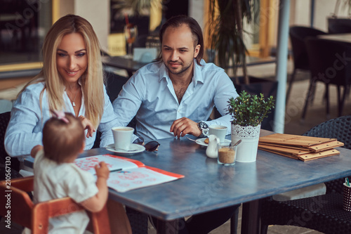 Family and people concept - happy mother, father and the little girl in outdoor cafe.