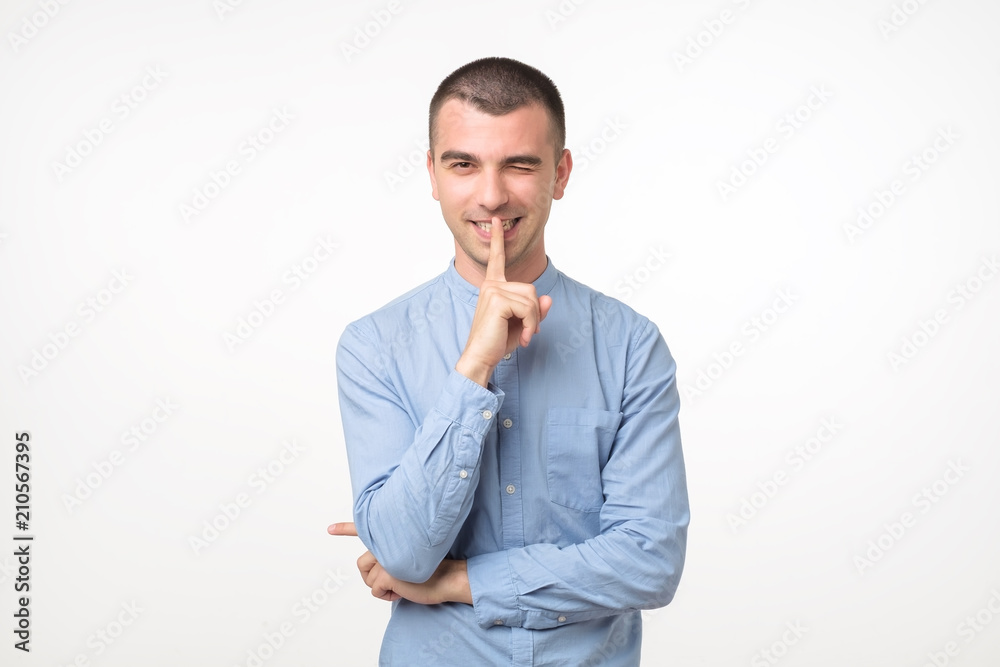 Young latin man in blue shirt keeps fore finger on lips, tries to keep conspiracy. Try to keep secrets. Young latin man in blue shirt keeps fore finger on lips, tries to keep conspiracy. Try to keep secrets.