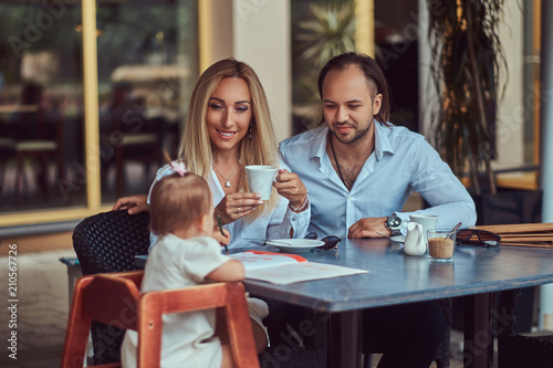 Family and people concept - happy mother, father and the little girl in outdoor cafe. © Fxquadro