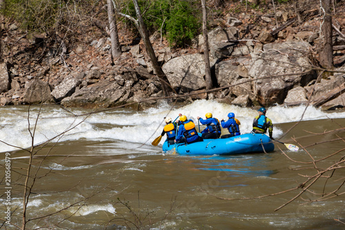 Rafters braving white water rapids in the early spring in a blue inflatable boat.