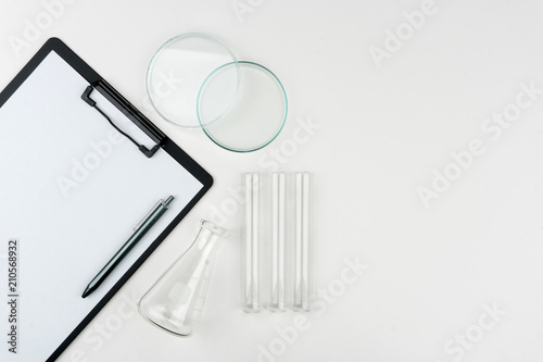 top view of laboratory equipments. A clipboard with pen, flask, test tubes and watch glass on the table