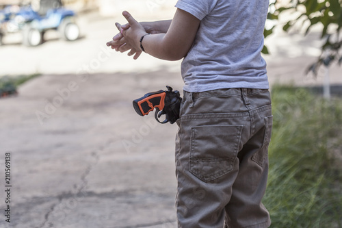 Little boy with plastic gun in the jeans pocket. Happy boy with toy pistol gun playing at outdoors in summer day.