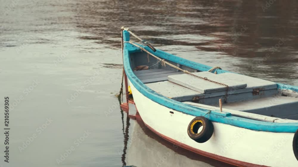 The old wooden fishing boat at the moorage of the seaport fluctuates, drifting on the water with small waves at sunset of a sunny day The old wooden fishing boat at the moorage of the seaport fluctuates, drifting on the water with small waves at sunset of a sunny day
