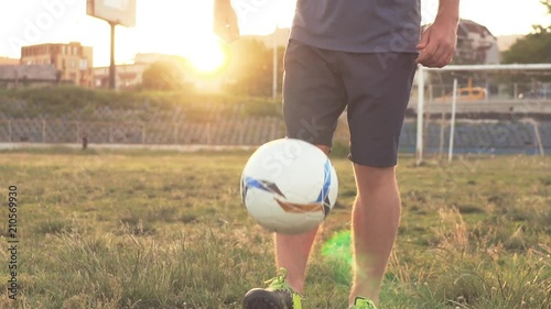 Slow motion football stunts. The football player throws the ball alternately with his feet. A teenager is playing on an abandoned football field at sunset on a sunny day in the summer. Football field