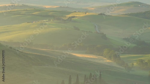 View of misty hilly Tuscan field with a farm and Cypresses in the evening golden hour at Valdocia in central Italy photo