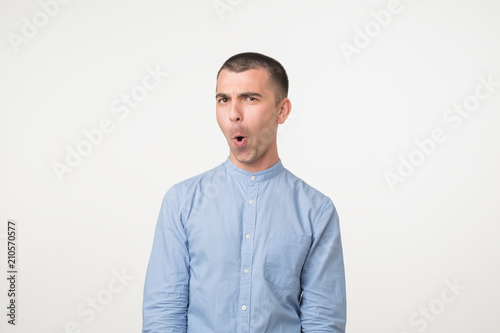 Shocked face of caucasian young man in blue shirt on grey background