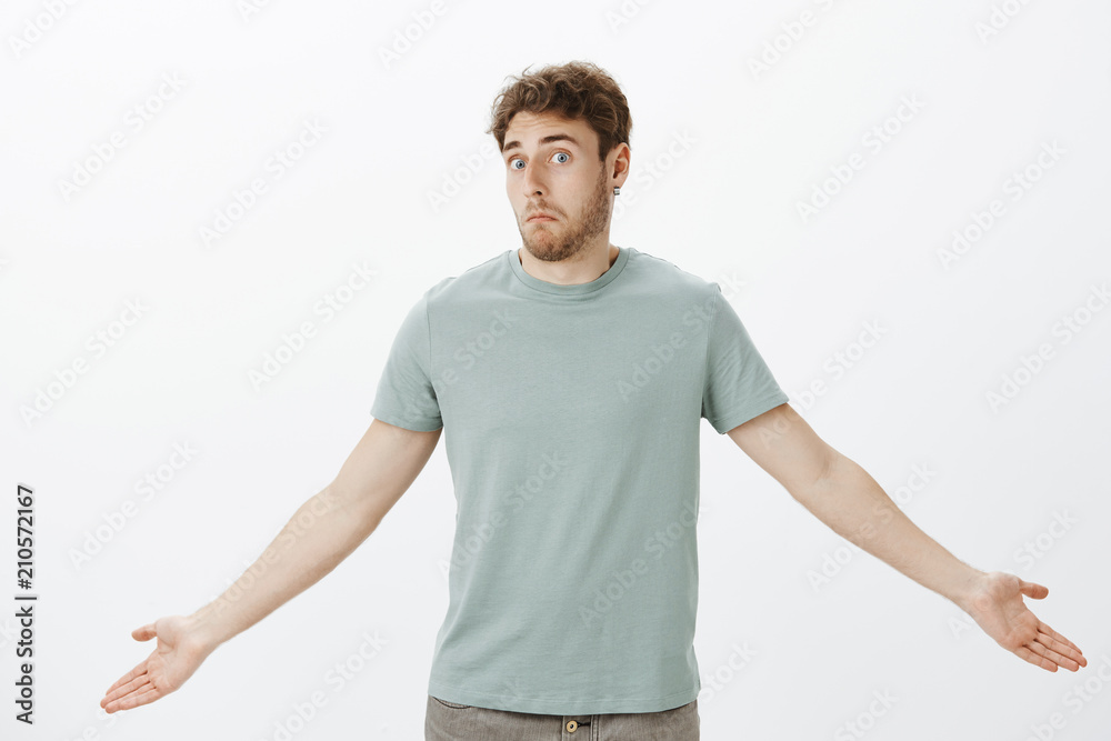 Guy feeling confused after loosing wallet. Portrait of questioned timid attractive man in t-shirt, spreading palms and shrugging with awkward unaware expression, having no idea what happened Guy feeling confused after loosing wallet. Portrait of questioned timid attractive man in t-shirt, spreading palms and shrugging with awkward unaware expression, having no idea what happened