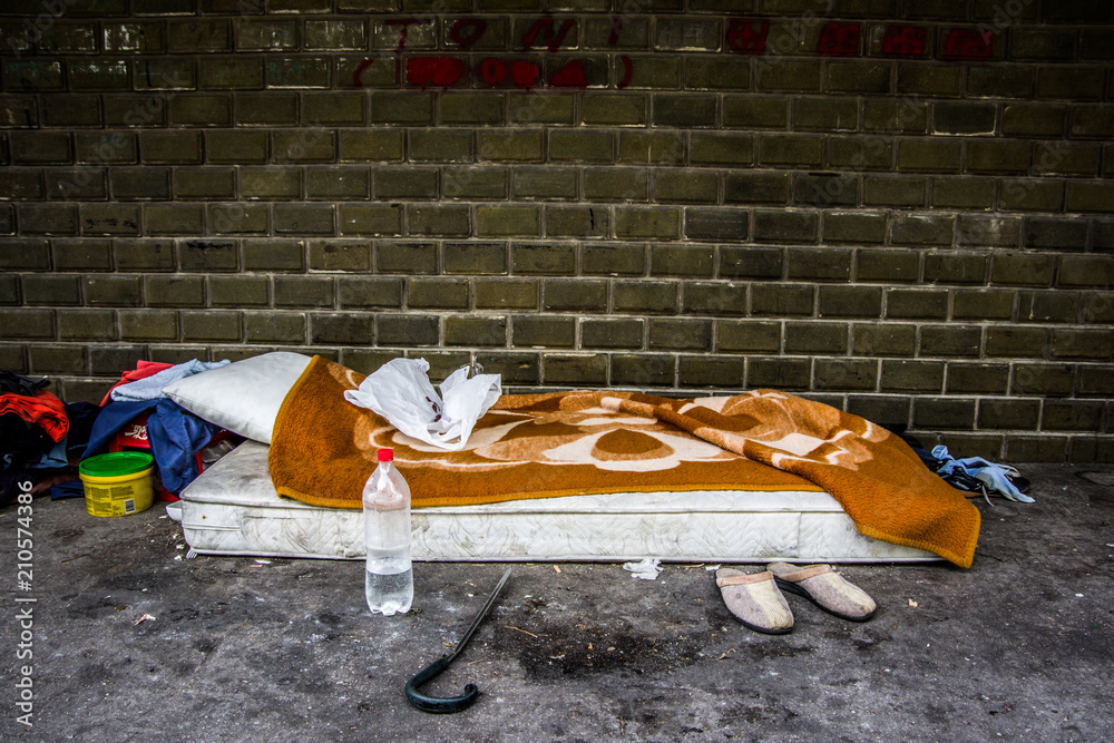 Side view of homeless men bed and an orange blanket. Belongings in the front.