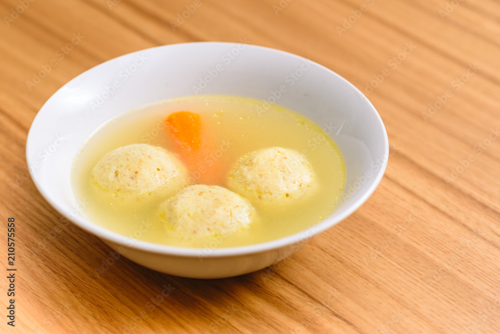 Traditional matzoh ball (kneidlach) soup.White bowl with authentic matzo ball chicken taste hot soup ( bouillon ) tradition Jewish food for Passover and every day. Traditional matzoh ball (kneidlach) soup.White bowl with authentic matzo ball chicken taste hot soup ( bouillon ) tradition Jewish food for Passover and every day.