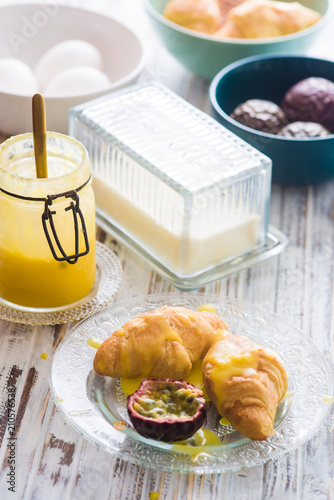 Passion fruit curds over small french croissant with split passion fruits and some bowl of ingredients to make the curds: butter,egg,sugar and passion fruit