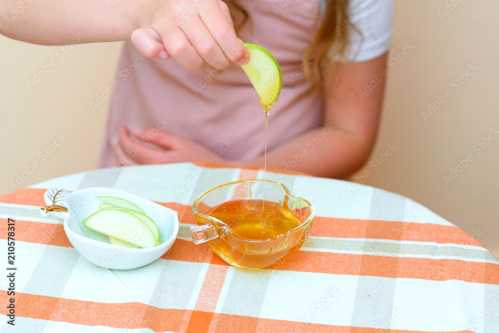 Close up of hands little girl eat apple with honey indoor. Jewish child dipping apple slices into honey on Rosh HaShanah the Jewish New Year. Close up of hands little girl eat apple with honey indoor. Jewish child dipping apple slices into honey on Rosh HaShanah the Jewish New Year.