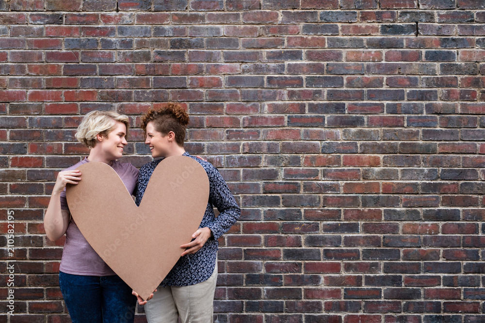 Content young lesbian couple standing outside together holding a heart