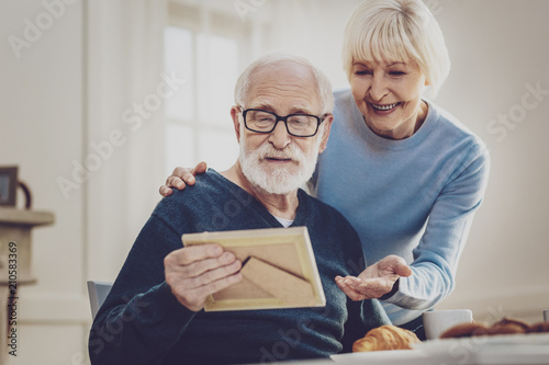 Look at it. Joyful aged woman pointing at the photo while looking at it together with her husband