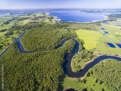 Meander of Wegorapa river flowing across wetlands, Mazury, Poland. Mamry Lake in the background