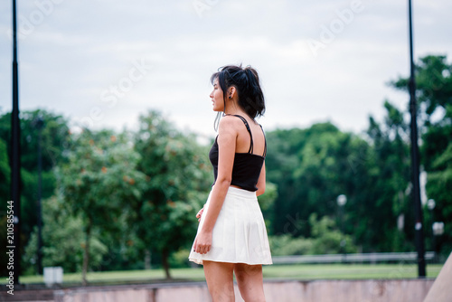 An portrait of a very attractive Chinese Asian girl enjoying her day under the sun. She is wearing a tank top and a white skirt. She is pretty, sporty, and attractive. 