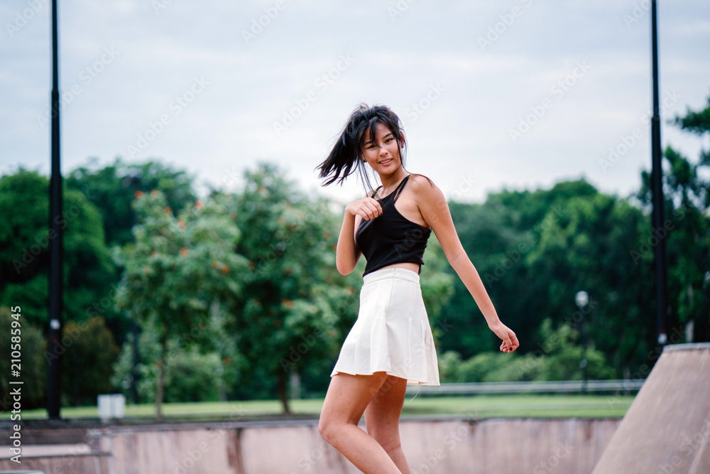 A portrait of a young Chinese Asian teenager in the skate park during the day. She is enjoying and smiling playfully as she whirls and twirls for a photograph.