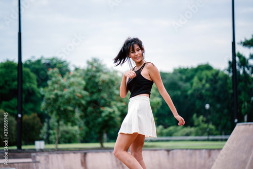 A portrait of a young Chinese Asian teenager in the skate park during the day. She is enjoying and smiling playfully as she whirls and twirls for a photograph. © Danon