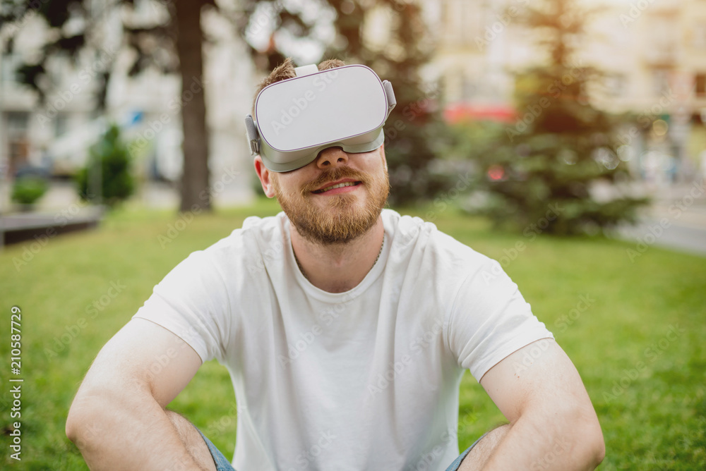 A young man plays a game wearing virtual reality glasses on the street.