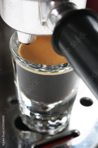 Espresso shot glass full of coffee with crema underneath an espresso machine