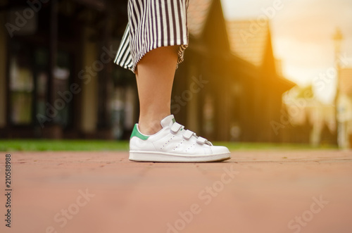 Female legs in street sneakers nature sun skyon blur background beauty fashion photo