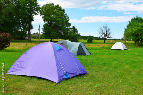 Three tents on meadow with green trees on background in sunny summer day with copy space for text on grass. Traveling  camping and hiking concept.