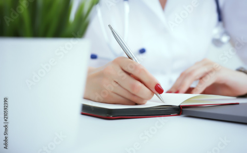 Female medicine doctor hand holding silver pen writing something on clipboard and working laptop closeup. Physician ready to examine patient and help
