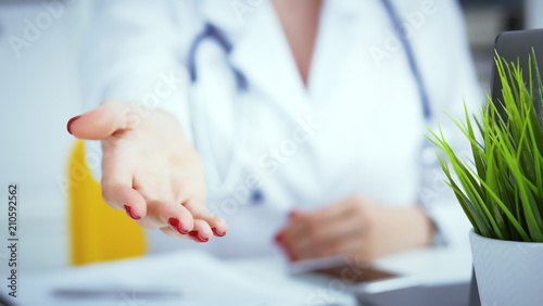 Female doctor making welcome gesture, politely inviting patient to sit down in medical office. Photo with depth of field.