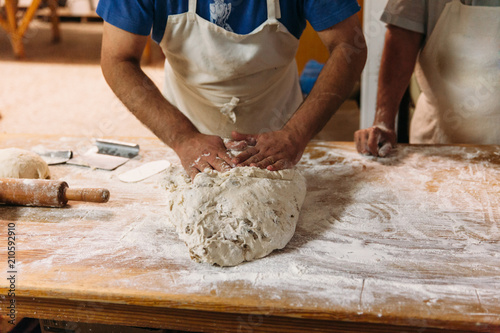 Baker is kneading dough to prepare bread on a rustic table in a bakery. Traditional Bakery Concept.