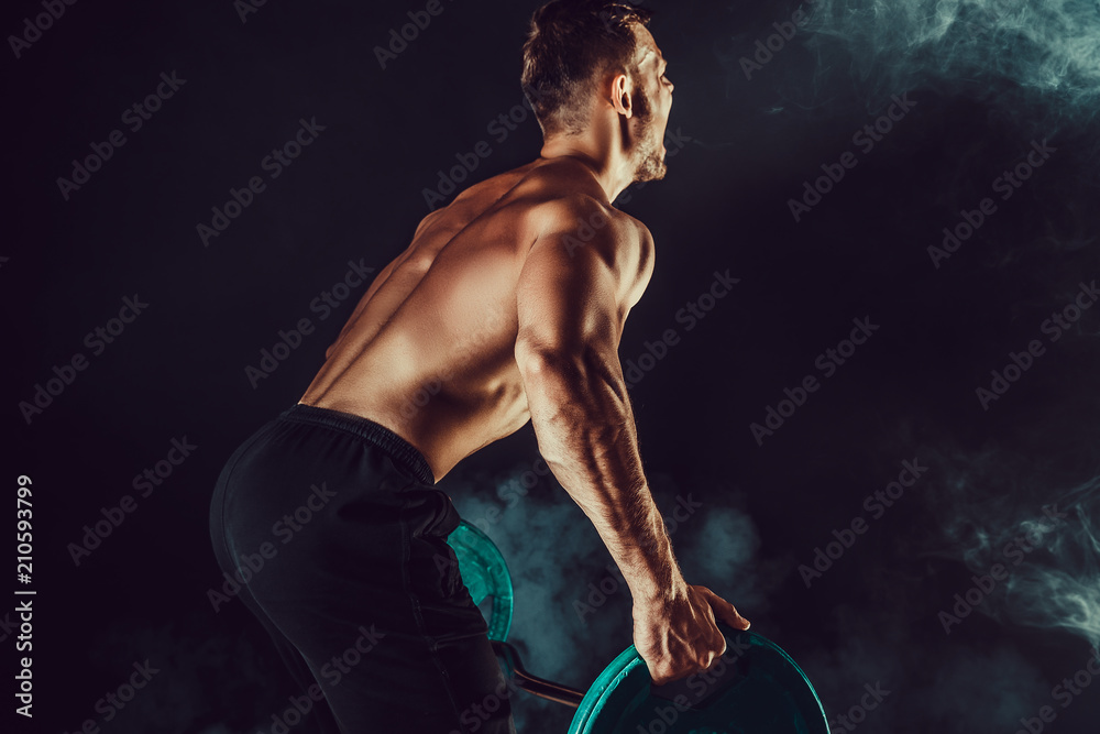 Strong athletic man pumping up muscles workout bodybuilding. muscular bodybuilder handsome men doing exercise for muscles of back with a barbell on dark background with smoke. Strength and motivation.