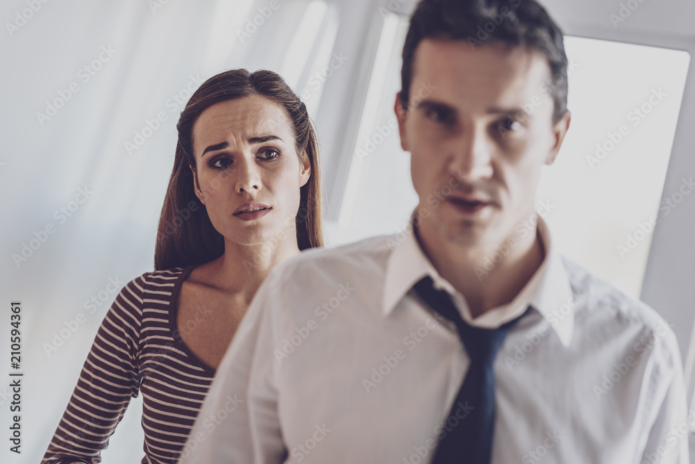 Family problems. Unhappy cheerless woman looking at her husband while having problems in relationships with him Family problems. Unhappy cheerless woman looking at her husband while having problems in relationships with him
