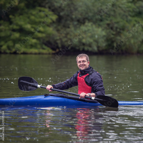 Young athletic man sits in a sports kayak boat smiling on a wide river.