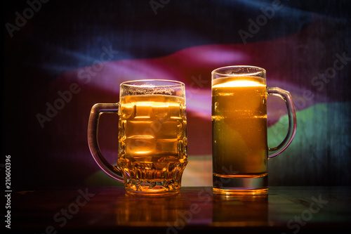 Creative concept. Beer glasses on table at dark toned foggy background with blurred view of flag of Germany.