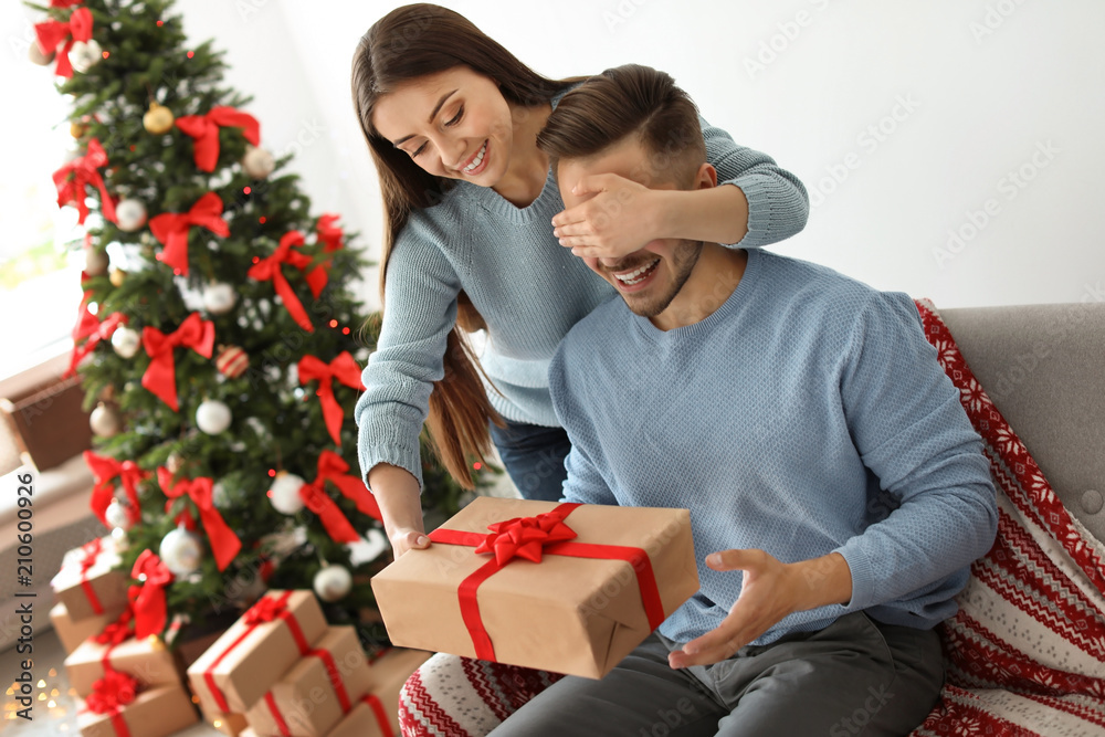 Young woman surprising her boyfriend with Christmas gift at home Young woman surprising her boyfriend with Christmas gift at home