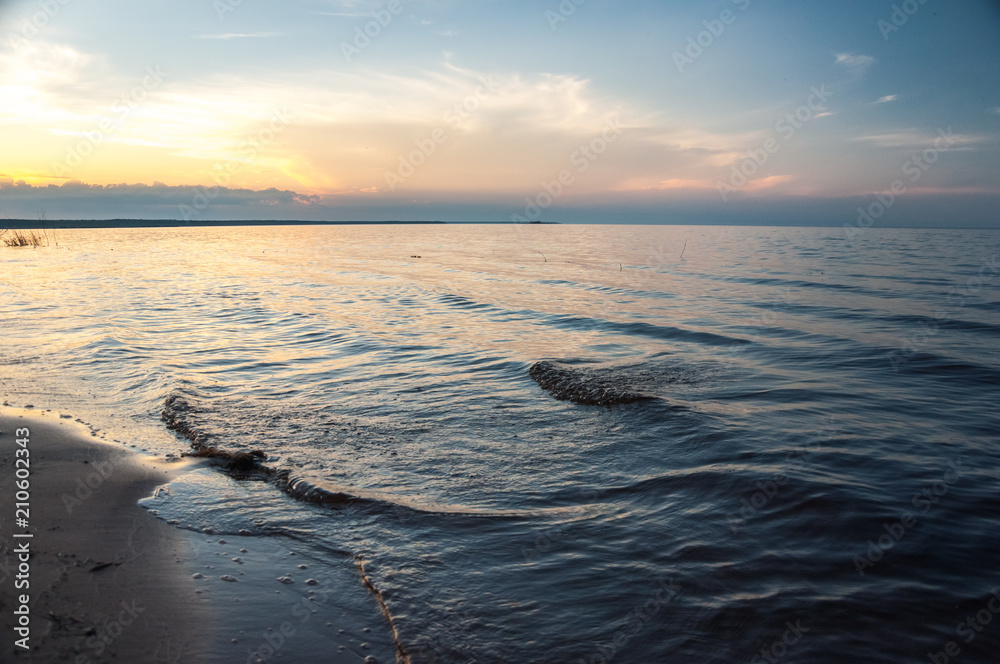 Naklejka premium Sea waves on the sandy beach in sunset. Ladoga lake