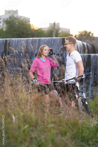 sport Concepts. Pair of Positive Caucasian Mountain Bikers Posing Together Outdoors With Bikes. Waterfall on Background.