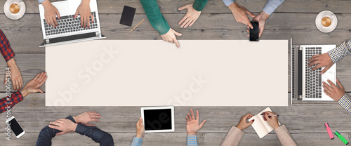 Business Teamwork concept - top view of eight business people. White blank sheet of paper in the middle of the wooden table.