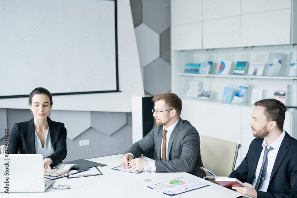 Group of three modern entrepreneurs sitting at meeting table in conference room and discussing startup projects, copy space Group of three modern entrepreneurs sitting at meeting table in conference room and discussing startup projects, copy space