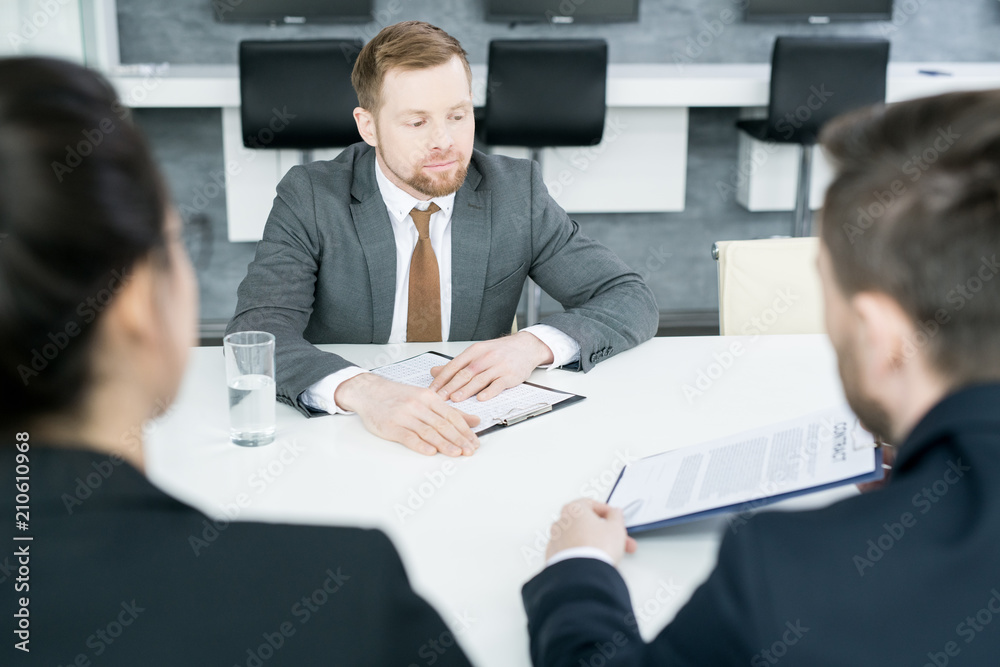 Portrait of modern young businessman reading contract from partners while sitting at meeting table in conference room, copy space Portrait of modern young businessman reading contract from partners while sitting at meeting table in conference room, copy space