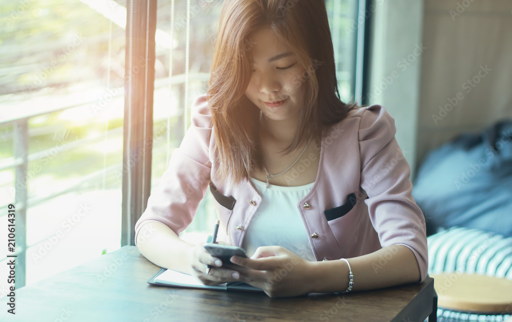 Obraz premium beautiful business lady in smart casual wear is holding a pencil,with mobile phone. and smiling while sitting at the desk in office